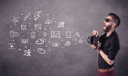 An elegant hipster guy trying to use a vintage camera with camera settings icons drawn on wall, like flash, white balace or ISO value concept