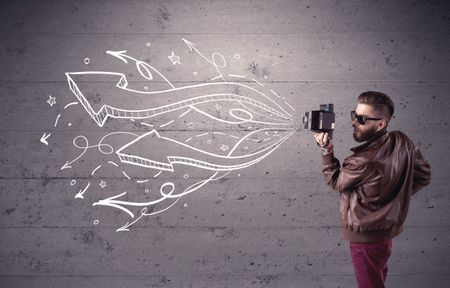 A hipster guy opening his point of view through looking a vintage camera concept with illustratied drawn arrows on urban wall