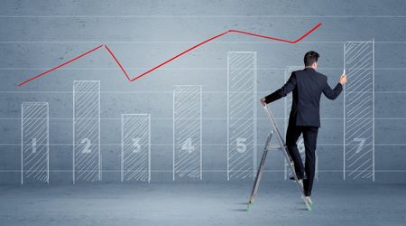 A man in elegant suit standing on a small ladder and drawing a chart on blue wall background with numbers, lines, blocks,