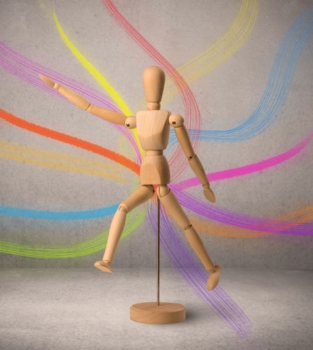 Wooden mannequin posed in front of a greyish background with colorful lines behind it