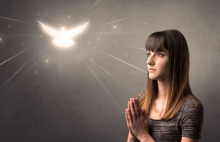 Young woman praying on a grey background with a sparkling bird above her