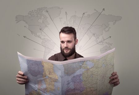 Handsome young man holding a map with world map and arrows behind him