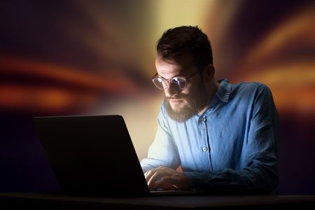 Young handsome businessman working late at night in the office with warm lights in the background