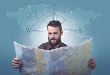 Handsome young man holding a map with a world map and a compass behind him