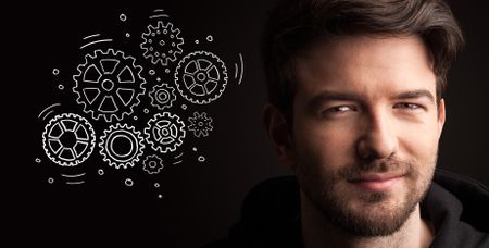 Portrait of a young businessman with rotating gears next to him on a dark background