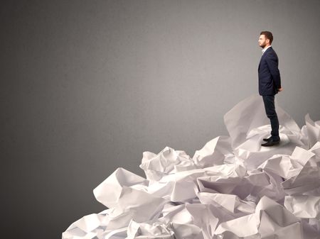 Thoughtful young businessman standing on a pile of crumpled paper with a deep grey background