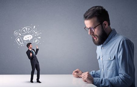 Young professional businessman being angry with an other miniature businessman who has drawn speech and thought bubbles above his head