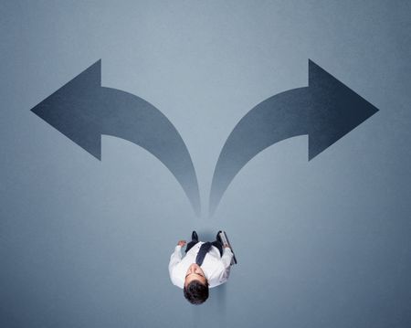 Young smart businessman standing in front of two arrows potinting to different ways contemplating a decision