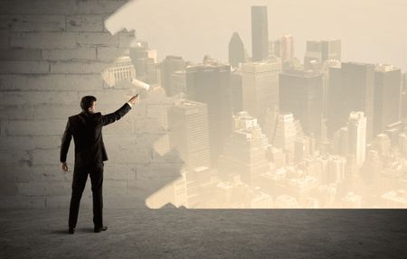 An elegant businessman with a paint roller transforming a brick wall into urban city landscape including tall buildings concept