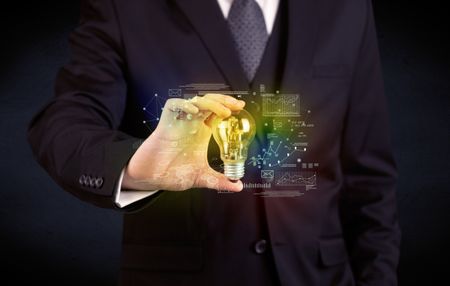 A serious business person has a complex solution concept illustrated by glowing glass light bulb in his hand with graph charts, numbers, lines, calculations.