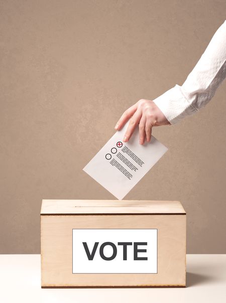 Close up of male hand putting vote into a ballot box, on grungy background
