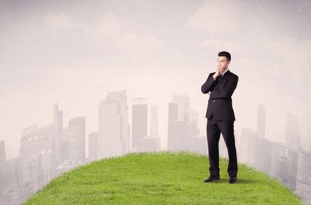 A confident male well looking office manager standing in small green grass in front of city landscape with tall buildings concept.