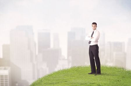 A cheerful caucasian elegant sales manager standing in small green grass in front of faded city landscape, tall buildings concept.