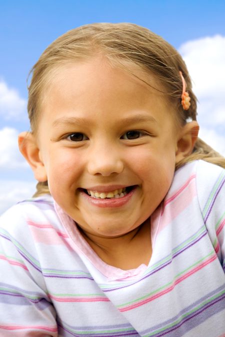 little girl portrait outdoors smiling over a wblue sky in the background