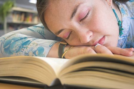 Beautiful student sleeping over a book on the libray.