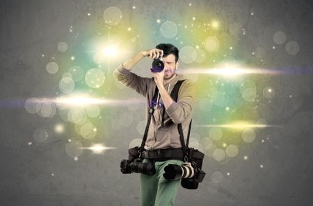 A young amateur photographer with professional camera equipment taking picture in front of grey wall full of colorful bokeh and glowing lights concept