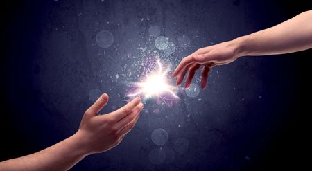 Two male hands reaching towards each other, almost touching with fingers, lighting spark in galaxy background concept