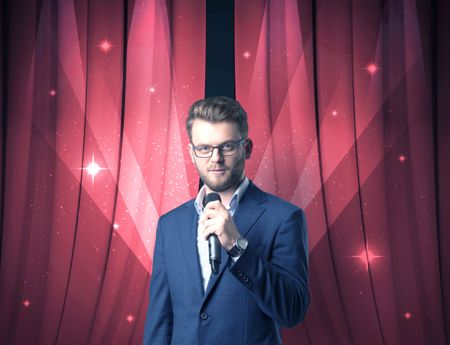 Businessman speaking into microphone with red curtain behind him 