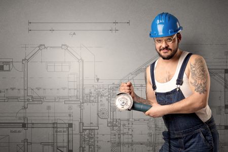 Worker standing with tool in his hand in front of technical drawings.