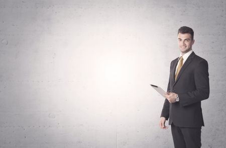 Young sales business person in elegant suit standing in front of clear empty grey wall background while talking on the phone