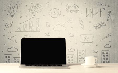 An open laptop on a white office desk with flower, coffee, books in front of wall background full of financial business charts concept