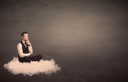 Caucasian businessman sitting on a white fluffy cloud wondering with a plain grunge background