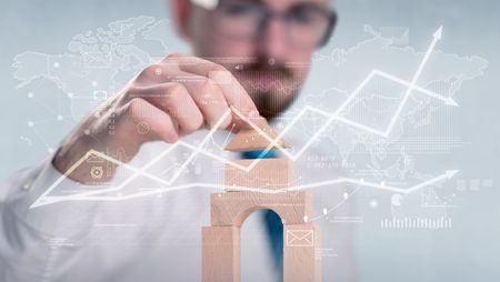 Young handsome businessman using wooden building blocks with data and calculations behind him