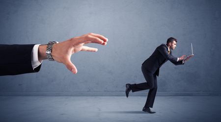 Young miniature businessman running from a big hand with blueish background