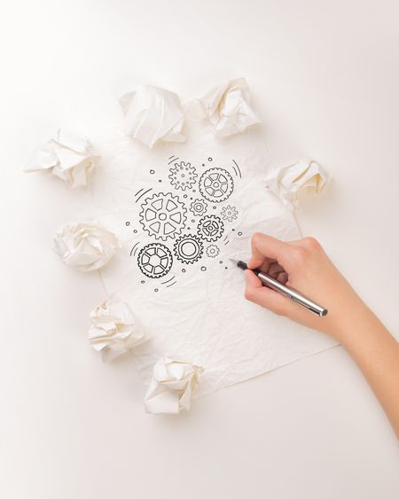 Female hand next to a few crumpled paper balls drawing rotating gears