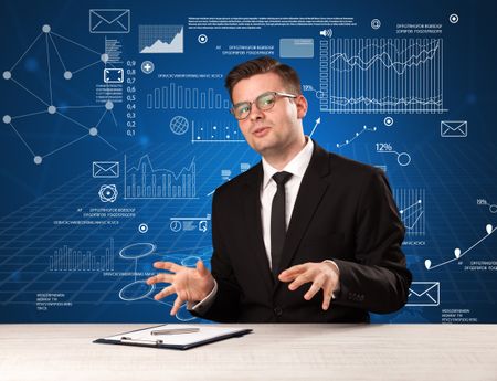 Young handsome businessman sitting at a desk with blue charts and data behind him