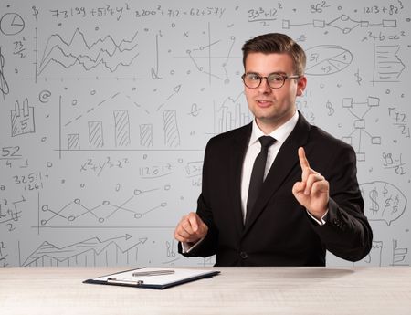 Young handsome businessman sitting at a desk with white charts behind him