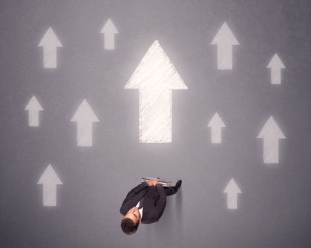 Young contemplating businessman stands in front of white arrows