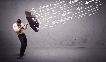 Business man standing with umbrella and drawn arrows hitting him on grungy background