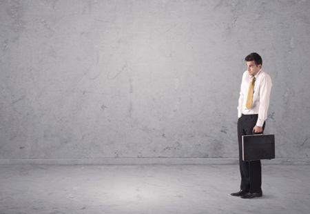 A surprised young sales person in elegant suit standing in empty urban environment with grey concrete wall background concept