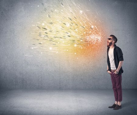 A young hipster guy with beard and sunglasses shouting in front of urban wall with vomit like colorful paint splatter on wall concept