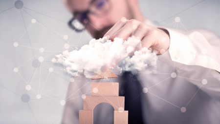 Young handsome businessman using wooden building blocks behind cloud concept 