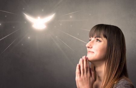 Young woman praying on a grey background with a sparkling bird above her