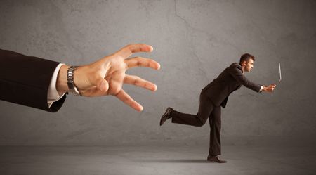 Young miniature businessman running from a big hand with grey background