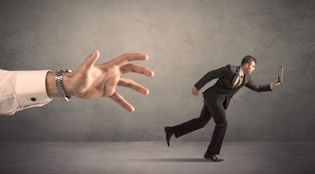 Young miniature businessman running from a big hand with grey background