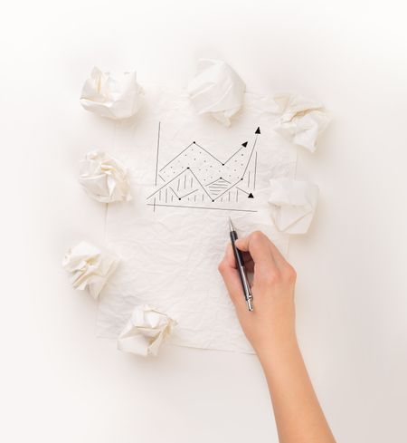 Female hand next to a few crumpled paper balls drawing a progress chart