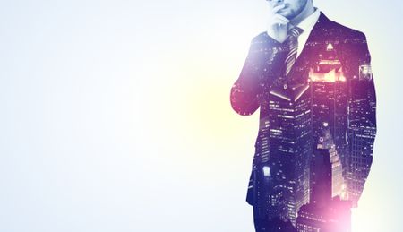 Young businessman thinking and standing with night skyscraper background
