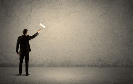 An elegant businessman in suit holding a paint roller, standing with his back, facing an empty urban concrete wall concept