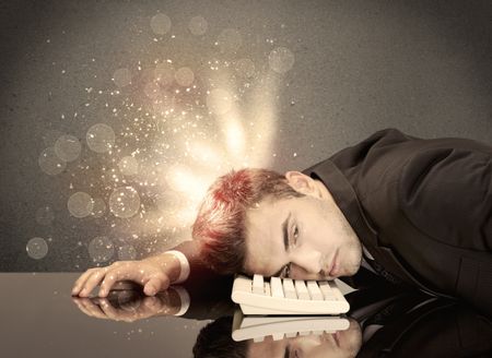 A young depressed business person laying his head on computer keyboard with thoughts exploding from his head illustrated by light beams concept