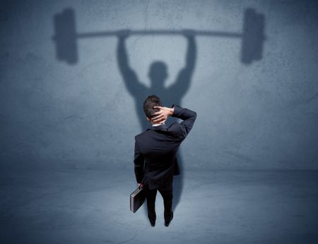 A confident young elegant salesman with briefcase facing a wall, looking at his strong, weight lifting shadow concept