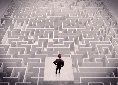 A confused businessman thinking while standing on a square platform above a detailed maze