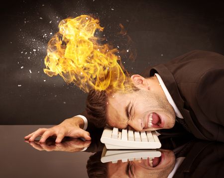 A depressed businessman banging his head in a keyboard and shouting with his head on fire, reflecting on desk