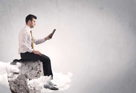 An elegant  smart businessman with laptop sitting in empty grey space on top of a cliff, between clouds concept