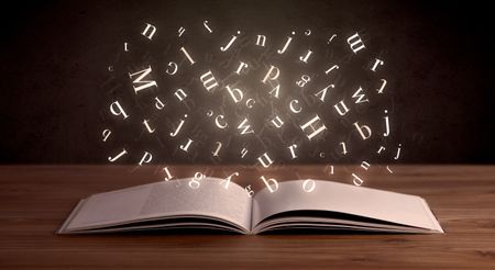 Glowing white alphabet letters coming out of an open book