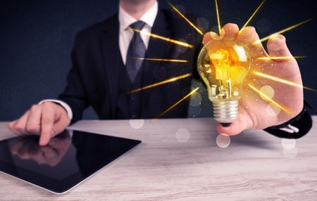 A male business person holding an electric light bulb in his hand with beam rays illustration concept.