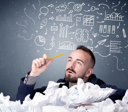 Young businessman sitting behind crumpled paper with mixed drawings over his head